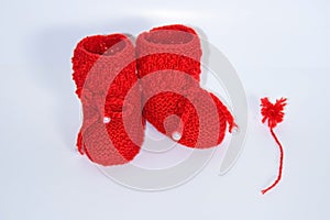 Red knitted baby booties and a red pompon of yarn on a white background