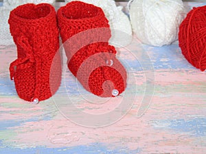 Red knitted baby booties, a red and white balls of wool yarn for knitting on a pink - blue background