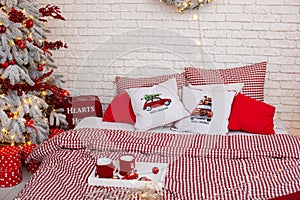 Red knitted cups of tea staying on wooden tray lies on bed. Winter holiday morning, cozy room. White Bedroom interior with checker