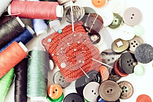 Red knitted needle pad for sewing, sewing buttons and colored thread coils on white background with copy space for text