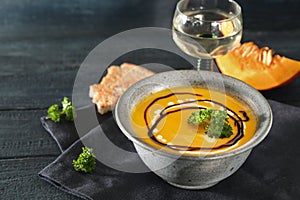 Red kuri squash soup with parsley garnish in a rustic blue bowl, white wine and bread on a dark wooden table, autumn meal for