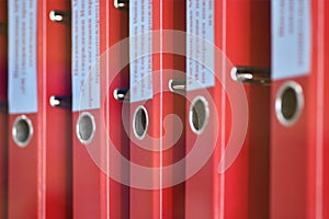 Red large folders files with inscriptions for storing office documents stand vertically on a shelf