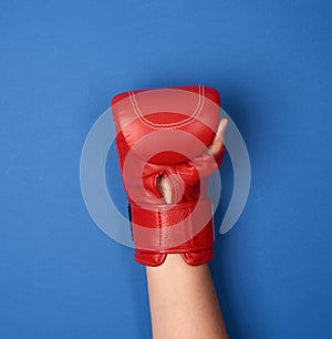 Red leather boxing glove on a female hand on a blue background