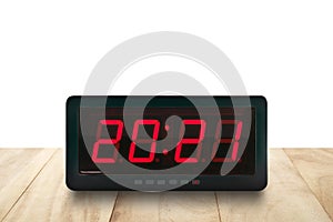 Red led light illuminated numbers 2021 on digital electric alarm clock face on brown wooden table isolated on white background