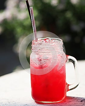 Red lemon soda water flavoured drink, Cool Drinks Beverages with ice in clear glass with paper and plastic straws on white table