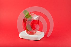 Red lemonade on red background, close-up. Glass of freshening summer soft drink with ice cubes