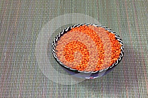 Red lentils in a ceramic cup standing on a straw mat