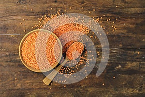 Red lentils in wooden plate and spoon on dark wooden table