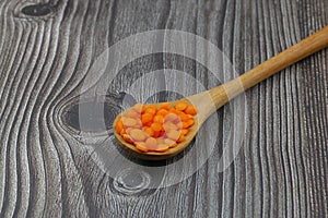 Red lentils in a wooden spoon on an old wooden table close-up. Vegetarian food