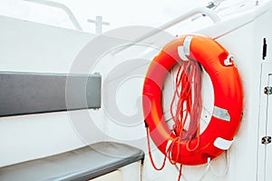 Red lifebuoy with rope hanging on an exterior wall of white painted siding at boat