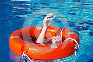 Red lifebuoy on the surface of the water in the pool and the hands of a man grabbing it