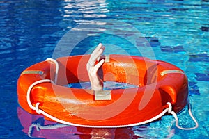 Red lifebuoy on the surface of the water in the pool and the hands of a man grabbing it