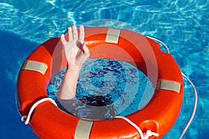 Red lifebuoy on the surface of the water in the pool and the hands of a man grabbing it