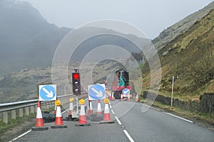 Red light at road works and traffic cones with safety sign at rural isolated mountain scene