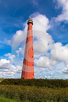 Red lighthouse in the harbor village den Helder against blue sky with cumulus clouds.