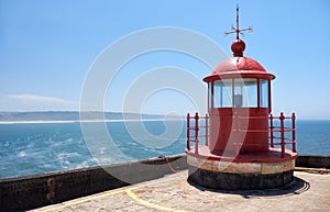 Red lighthouse lamp room on blue sky and sea background in Nazare, Portugal