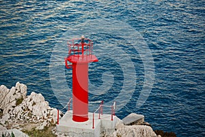 Red lighthouse on the rock cliff in the Adriatic sea water waves