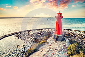 Red lighthouse on rocky harbor at sunset