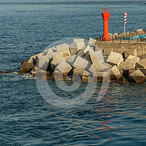 Red lighthouse surrounded by concrete blocks at the tip of the pier in the port of Los Christianos in Tenerife. View from the
