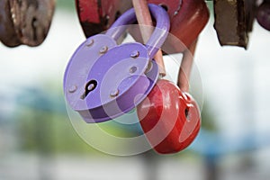 Red and lilac hearth locks of newlyweds hang on the handrail of the bridge lovers