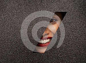 Red lips peep through a hole in shiny black paper. Beautiful white teeth