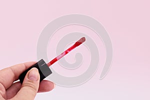 Red lipstick on the brush applicator with the black cap at the female hand on a pink background