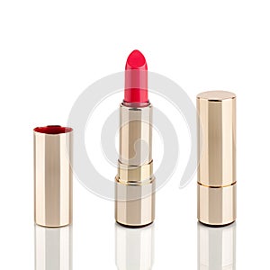 Red lipstick in golden tube on white background with mirror reflection on glass surface isolated close up, shiny gold lipsticks
