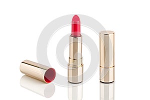 Red lipstick in golden tube on white background with mirror reflection on glass surface isolated close up, shiny gold lipsticks