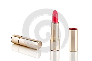 Red lipstick in golden tube on white background with mirror reflection on glass surface isolated close up, shiny gold lipsticks