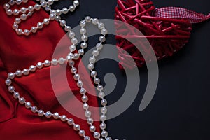 Red heart and lipstick, on a black background, a string of white pearls and a silk handkerchief