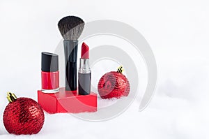 Red lipstick, nail polish, brush on podium on background of snow