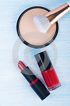 Red lipstick and nail polish next to blush and brush on a blue background