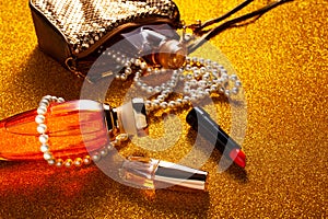 A red lipstick with orange perfume bottle and pearl necklace