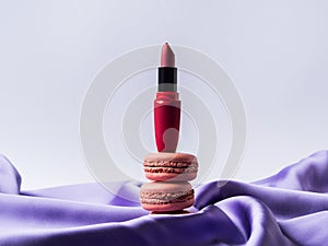Red lipstick and pink macaroons on purple silk fabric background
