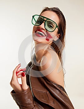 Red lipstick rubbed over. Beautiful young brunette girl with wet hair in stylish leather jacket smiling over grey studio