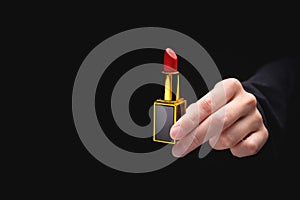 Red lipstick in a woman's hand on a dark background. Girl holding a popular cosmetic product
