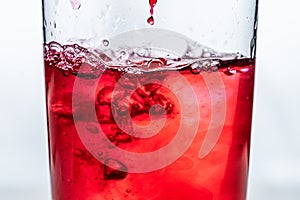 Red liquid being poured into a glass. White background.