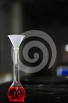 Red liquid in a round bottomed flask with funnel on a black granite table in dark background
