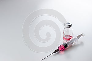 Red liquid vitamin B12 in a disposable syringe with a needle and in a glass ampoule on a white background.