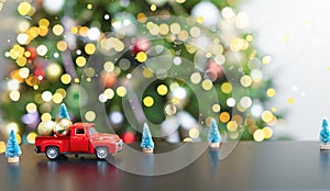 A red little car against the background of a defocus Christmas tree carries golden balls.