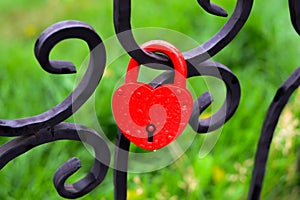 Red lock in the shape of a heart on a black fence, a symbol of love