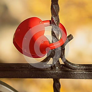 Red lock in shape of heart on black old metal fence, love symbol, selective focus, blurred background