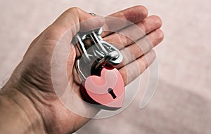 Red locked heart shaped padlock with steel chain in the male palm