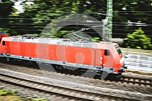 Red locomotive speeding through a green lush forest with the cables above