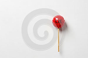 A red lollipop with LIE written on a light background. Space for text.