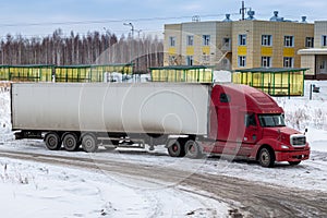 Red long-distance bonnet truck with a white semitrailer in the countryside