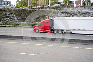 Red long haul big rig semi truck with broken fender transporting cargo in dry van semi trailer running on the city highway