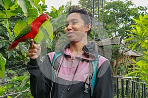 Red loryperching on the man hand. Asian handsome tenager with a parrot in a tropical bird park. Eos Bornea is a species