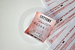 Red lottery ticket lies on pink gambling sheets with numbers for marking to play lottery. Lottery playing concept or gambling