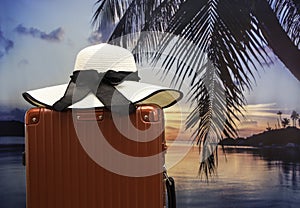 Red luggage with hat  on the beach which tropical palm and sunset sky scene background,Travel concept